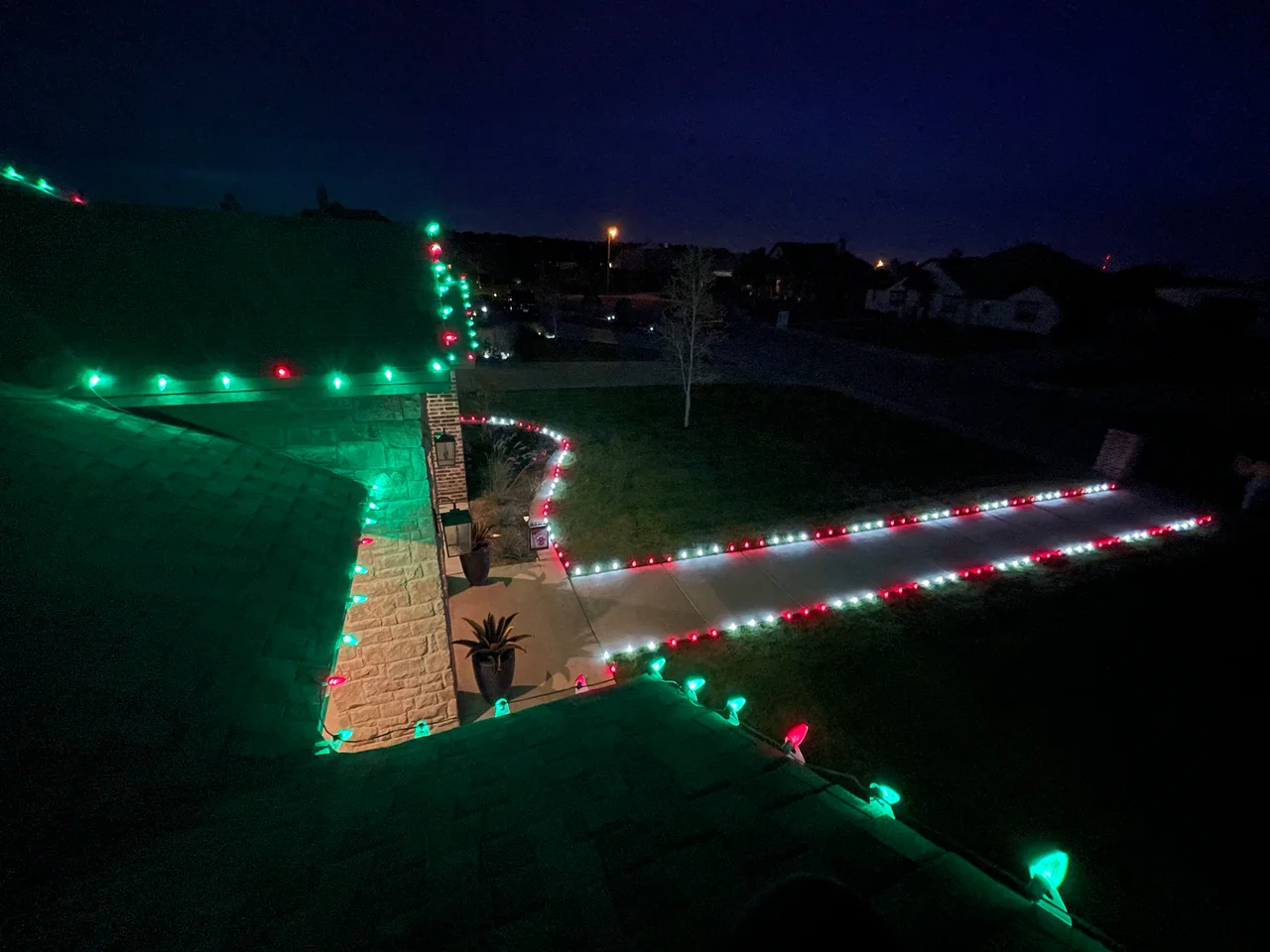Red-and-green roofline bulbs above a walkway edged in Christmas lights.