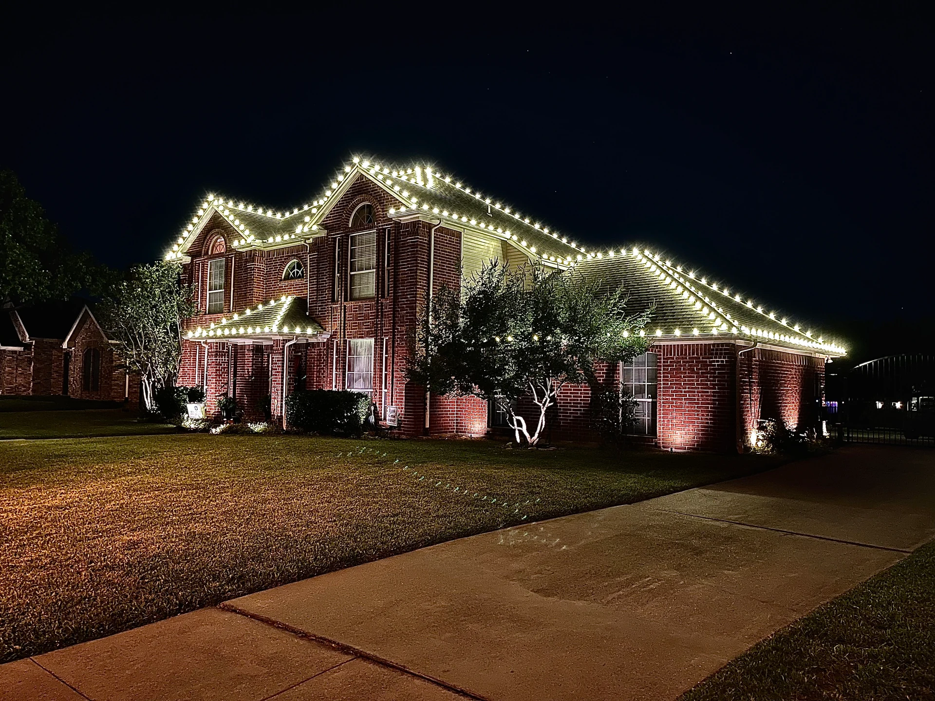 Warm-white Christmas lights outline the rooflines and peaks of a large two-story brick home.