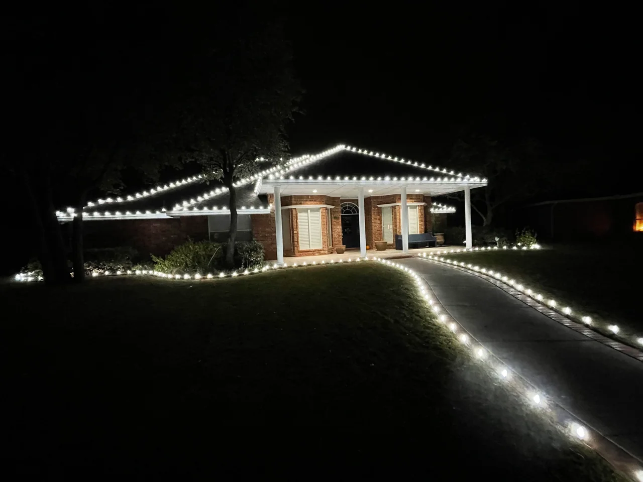 Cool-white Christmas lights trace a roofline and curved front walkway.