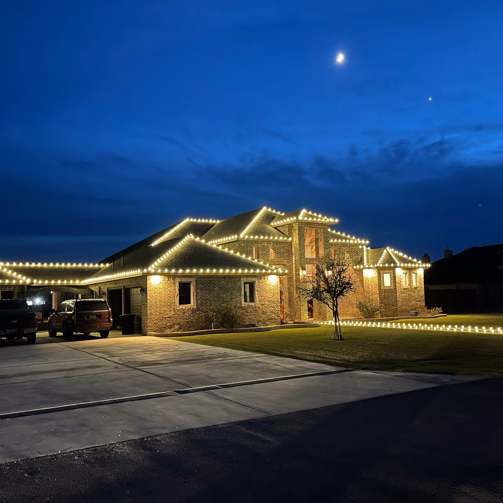 House outlined in warm white Christmas lights along its perimeter, ridgelines, and ground, radiating a cozy and festive ambiance.